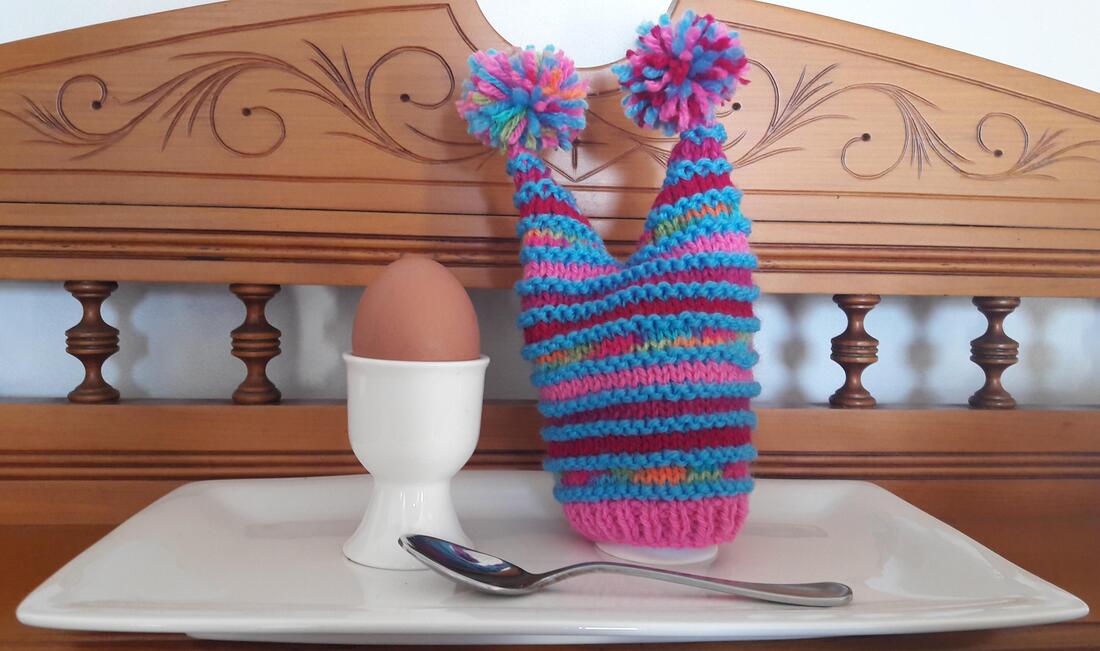Quirky double pointed knitted egg cup cosie in 8 ply with egg cups and spoon on tray