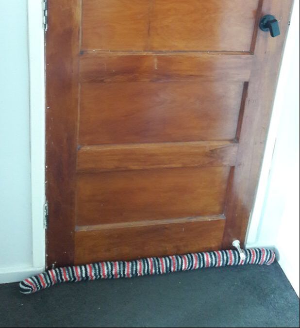 Striped knitted draught stopper in 8 ply placed against wooden Rimu door